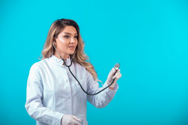 Femme médecin en uniforme blanc vérifiant avec stéthoscope et écoutant attentivement.