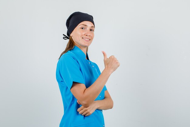 Femme médecin en uniforme bleu, chapeau noir montrant le pouce vers le haut et à la bonne humeur