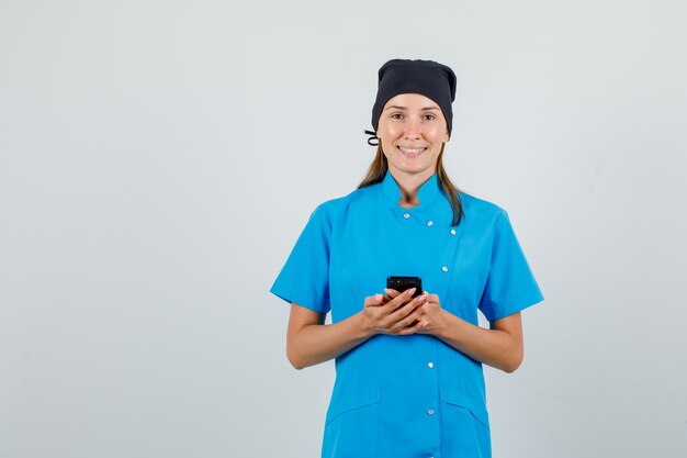 Femme médecin en uniforme bleu, chapeau noir tenant le smartphone et à la joyeuse