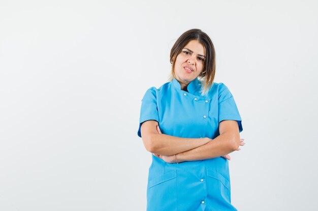 Femme médecin en uniforme bleu debout avec les bras croisés et l'air confiant.