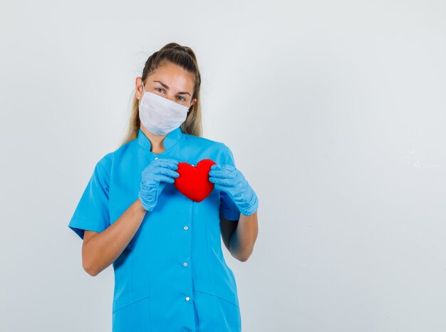 Femme médecin en uniforme bleu, masque, gants tenant un coeur rouge et à l'optimiste