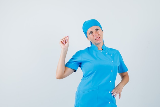 Femme médecin en uniforme bleu mesurant quelque chose de minuscule et regardant pensif, vue de face.