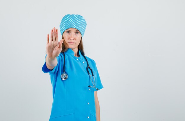 Femme médecin en uniforme bleu montrant le geste d'arrêt et à la grave, vue de face.