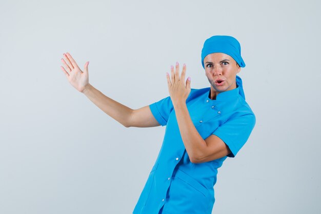 Femme médecin en uniforme bleu montrant le geste de karaté et l'air confiant, vue de face.