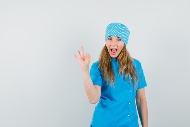 Femme médecin en uniforme bleu montrant le geste ok et à la recherche de plaisir