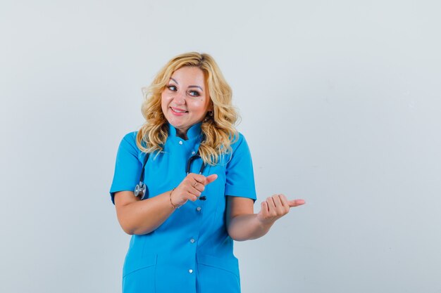 Femme médecin en uniforme bleu pointant de côté et à l'espace heureux pour le texte