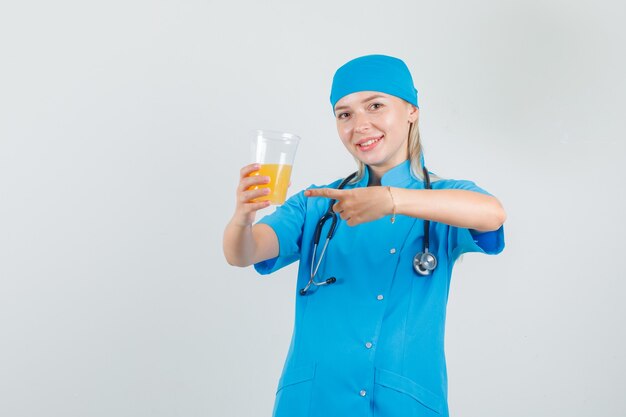 Femme médecin en uniforme bleu pointant le doigt sur le jus de fruits et à la bonne humeur