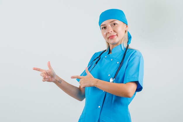 Femme médecin en uniforme bleu pointant vers le côté avec le geste du pistolet et à la bonne humeur