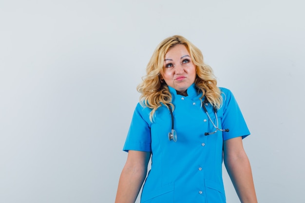 Photo gratuite femme médecin en uniforme bleu regardant ailleurs et à la recherche d'impuissance, de l'espace pour le texte