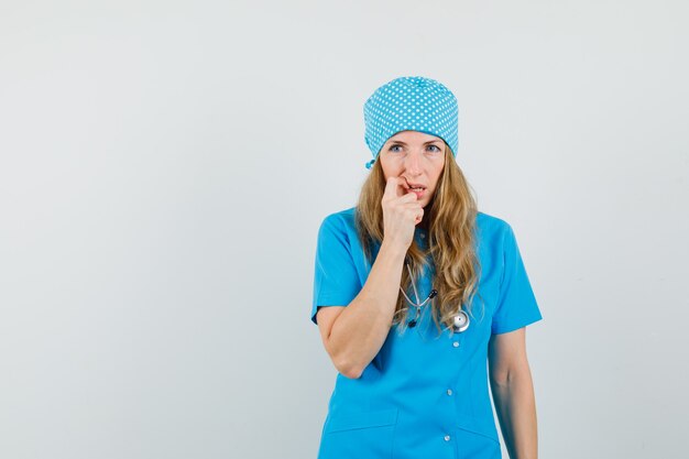 Femme médecin en uniforme bleu regardant ailleurs tout en pensant et à la recherche d'impuissance