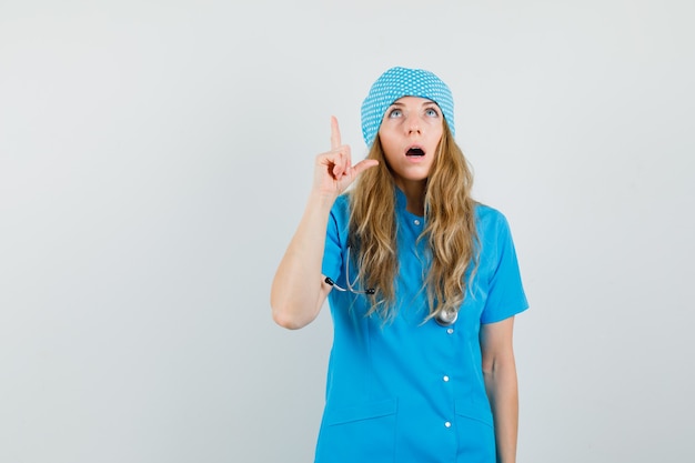 Femme médecin en uniforme bleu regardant avec le doigt vers le haut et à la surprise