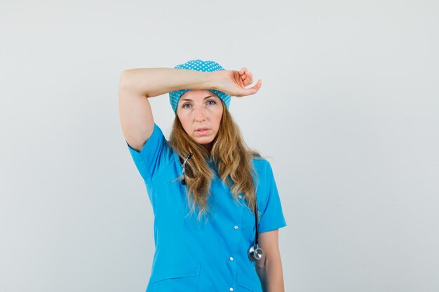 Femme médecin en uniforme bleu tenant le bras sur le front et l'air épuisé