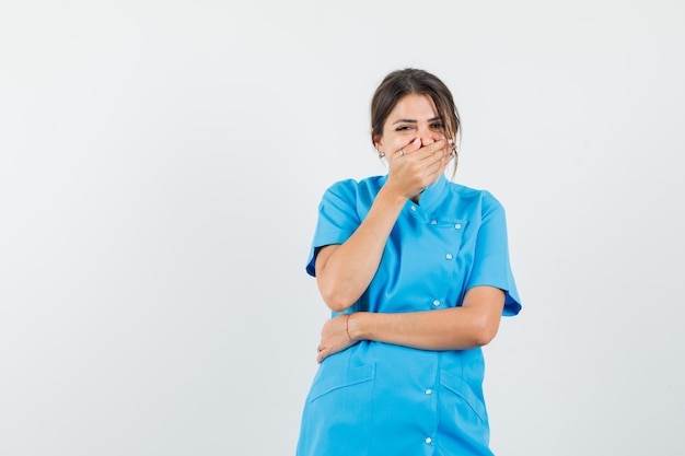 Femme médecin en uniforme bleu tenant la main sur la bouche et l'air heureux