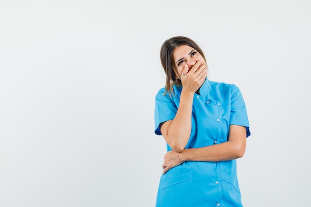 Femme médecin en uniforme bleu tenant la main sur la bouche et à la joie