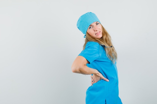 Photo gratuite femme médecin en uniforme bleu tenant les mains sur son dos et à la recherche de mal à l'aise.