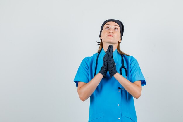 Femme médecin en uniforme, gants gardant les mains en geste de prière et à la recherche d'espoir