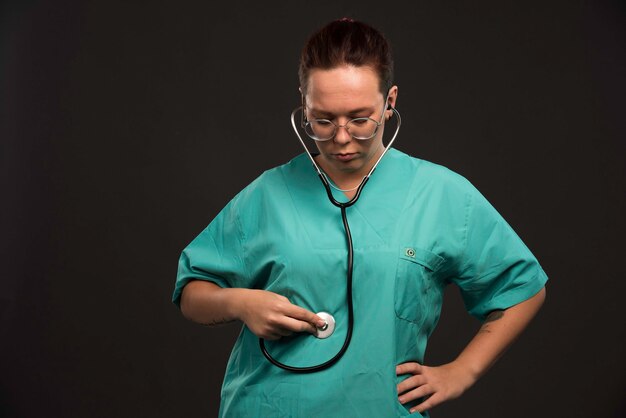 Femme médecin en uniforme vert tenant un stéthoscope et vérifiant son estomac.