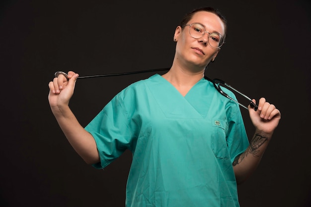 Femme médecin en uniforme vert tenant un stéthoscope.