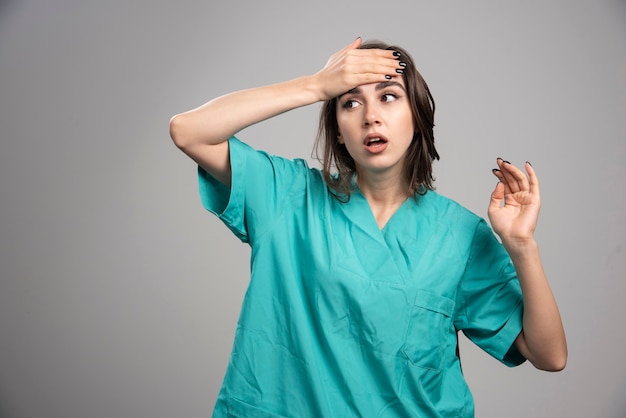 Femme médecin vérifiant sa température sur fond gris. Photo de haute qualité