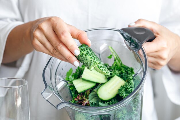 Une femme avec un mélangeur coupant du concombre pour un smoothie à la maison