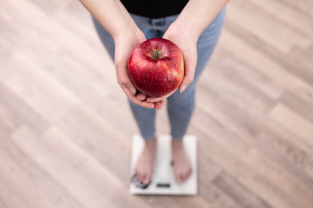 Une femme mesure le poids sur une balance, tient une pomme dans ses mains.