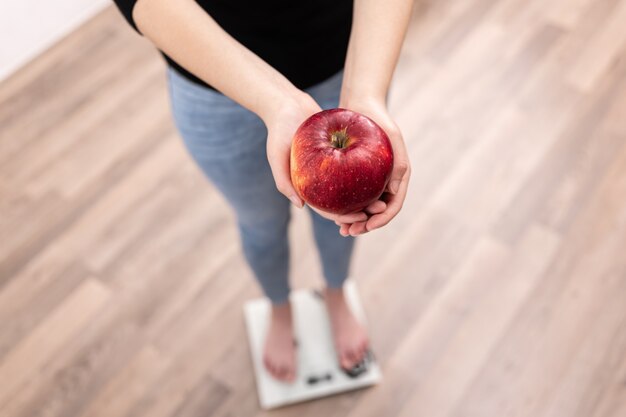 Une femme mesure le poids sur une balance tient une pomme dans ses mains