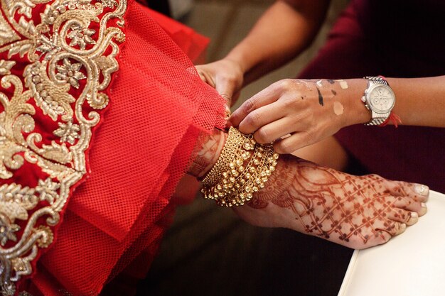 Femme met un bracelet en or avec des cloches sur la jambe de la mariée peint