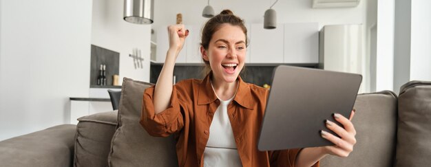 Photo gratuite femme mignonne excitée gagnant célébrant en regardant la tablette numérique et se réjouissant de la lecture triomphante