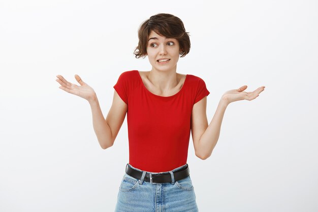 Femme mignonne maladroite et désemparée haussant les épaules indécise, à l'ignorance