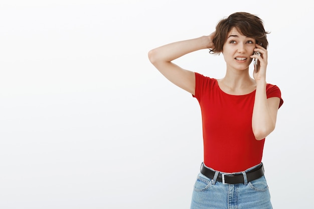 Femme Mignonne Maladroite Et Indécise Se Gratter La Tête Désemparée Tout En Parlant Au Téléphone