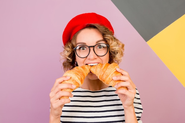 Femme mignonne rêveuse en béret rouge tenant de gros croissants savoureux dans les mains.