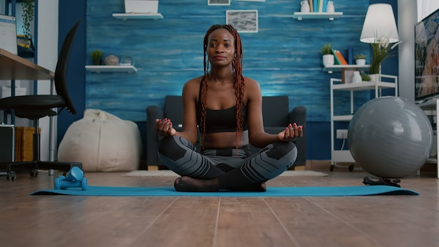 Femme mince d'athlète avec la peau foncée mettant en position de lotus sur la carte de yoga