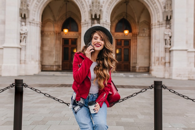 Photo gratuite femme à la mode avec une coiffure longue, parler au téléphone près d'un bâtiment historique étonnant en week-end