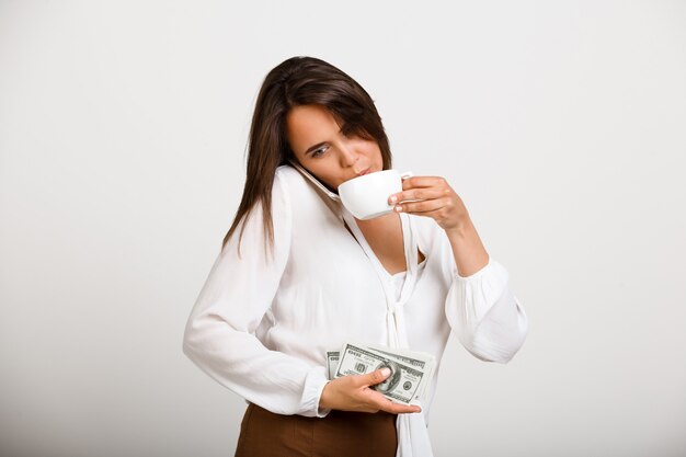 Femme de mode joyeuse, boire du café, garder de l'argent et parler au téléphone