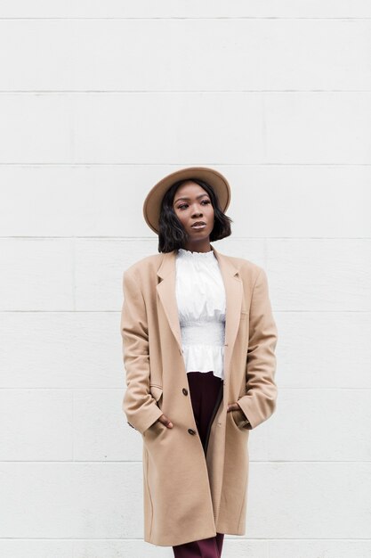 Femme à la mode posant à côté d'un mur blanc