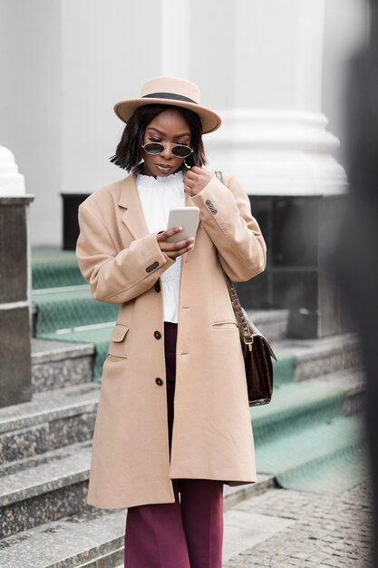 Femme à la mode à la recherche sur son téléphone à l'extérieur