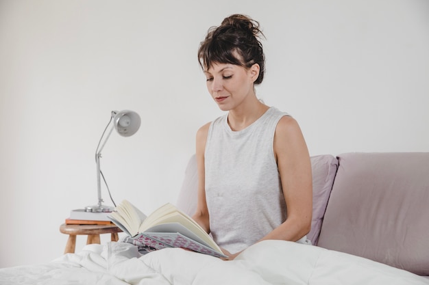 Femme moderne lisant dans le lit