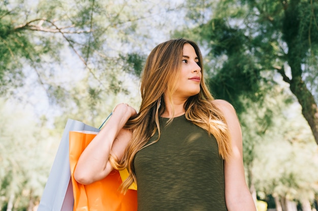 Photo gratuite femme moderne avec des sacs et des arbres à l'arrière-plan