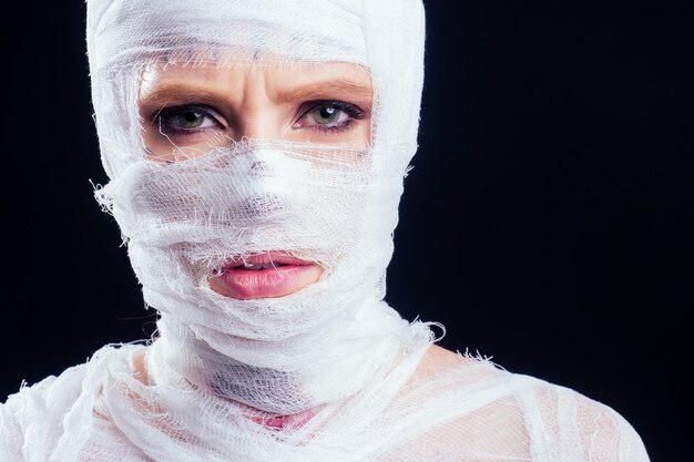 Femme momie glamour dans des bandages sur tout son corps sur fond noir de studio. fête d'halloween ou concept de victime de chirurgie plastique.