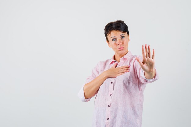 Femme montrant le geste d'arrêt en chemise rose et regardant anxieux, vue de face.
