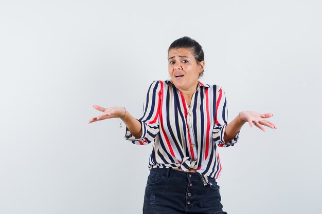 femme montrant un geste impuissant en chemise, jupe et à la confusion.