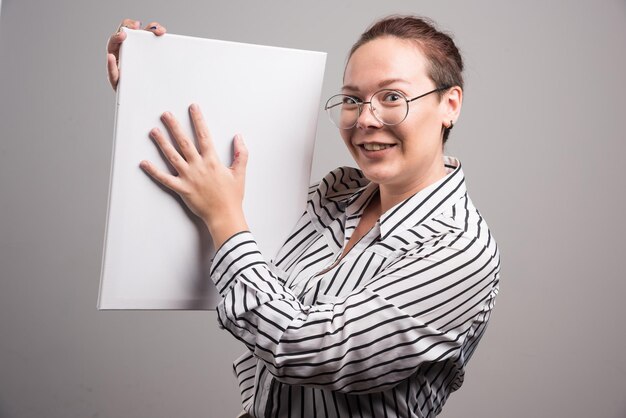 Femme montrant sa toile blanche vide sur gris