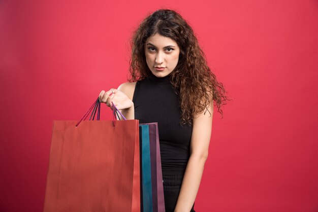 Femme montrant ses nouveaux vêtements d'achat sur fond rouge. Photo de haute qualité