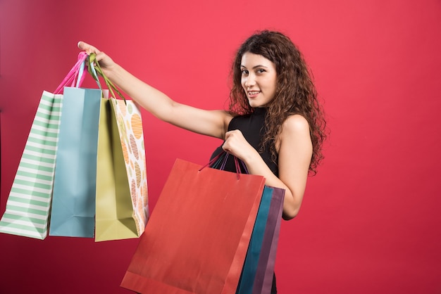 Femme montrant ses nouveaux vêtements d'achat sur fond rouge. Photo de haute qualité