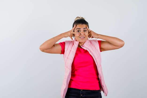 Femme montrant un signe V près de l'œil en t-shirt, gilet et à l'air excité