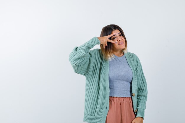 Femme montrant le signe V sur les yeux dans des vêtements décontractés et à la recherche de plaisir. vue de face.