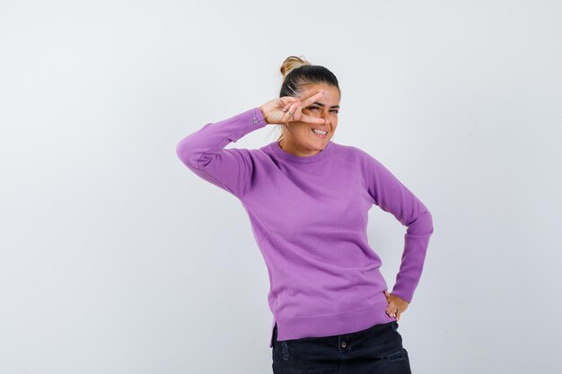 Femme montrant le signe de la victoire sur l'œil en blouse de laine et à heureux