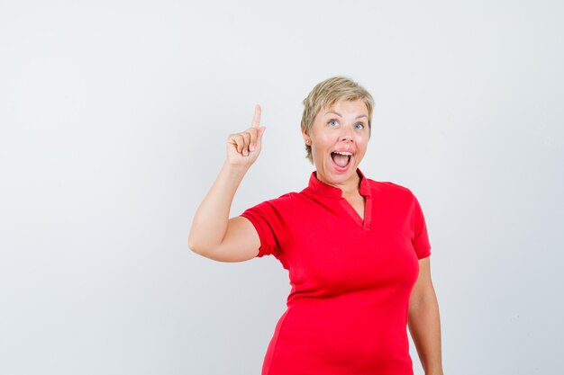 Femme mûre pointant vers le haut, ayant une excellente idée en t-shirt rouge.