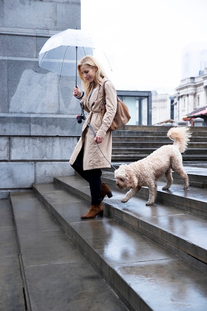 Femme mûre promenant son chien dans la ville pendant qu'il pleut