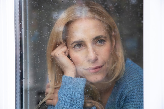 Femme Mûre Regardant à L'extérieur De Sa Fenêtre Pendant Qu'il Pleut Photo gratuit